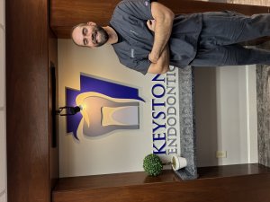 Dr. Cole wearing scrubs next to Keystone Endodontics sign